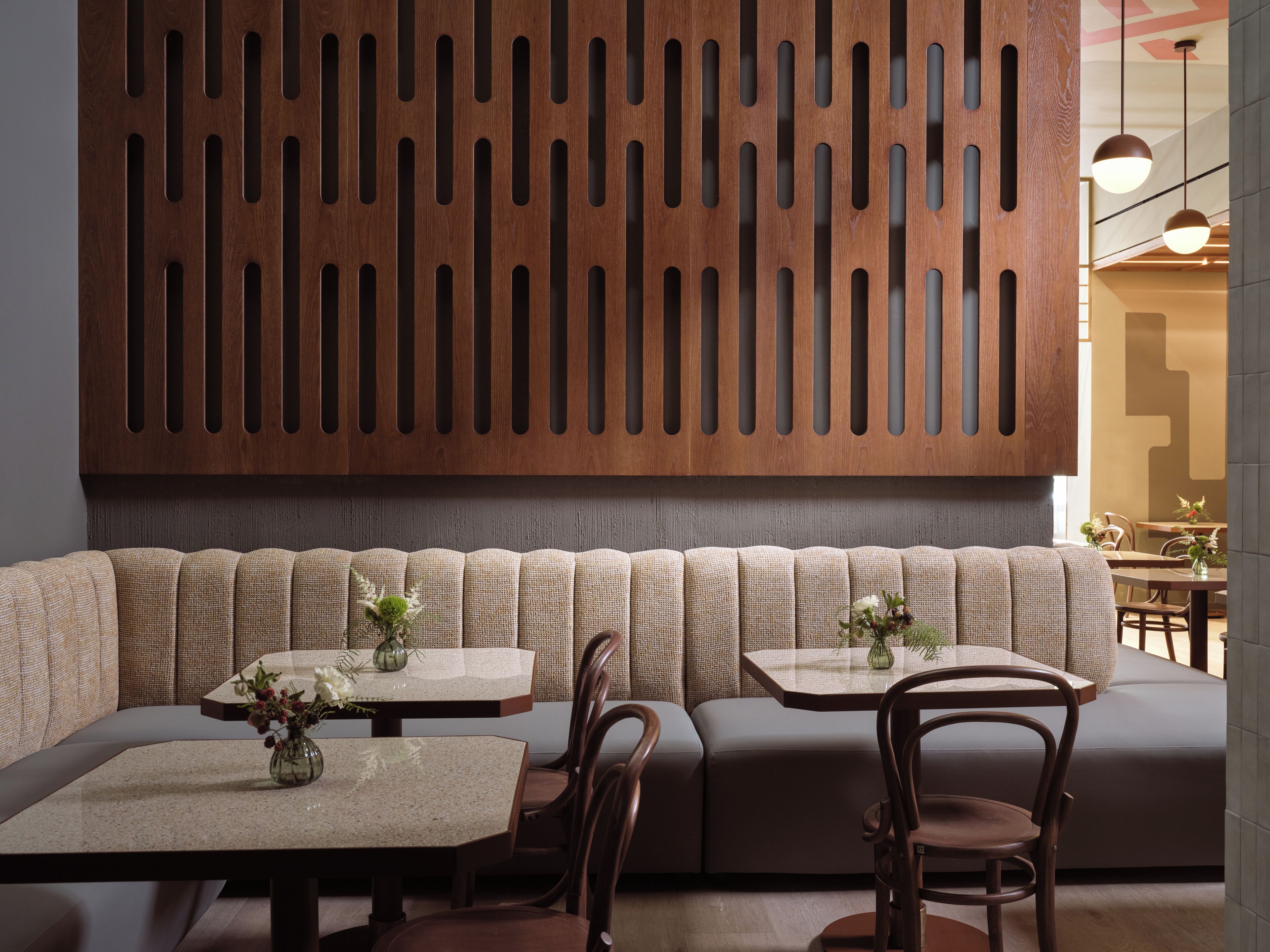 A modern interior with a wooden slat wall, cushioned seating, and tables with vases.