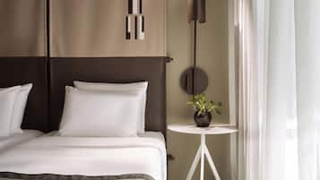 Una habitación de hotel moderna con una cama grande, una mesita de noche con una planta en maceta, un espejo redondo y una lámpara colgante.
