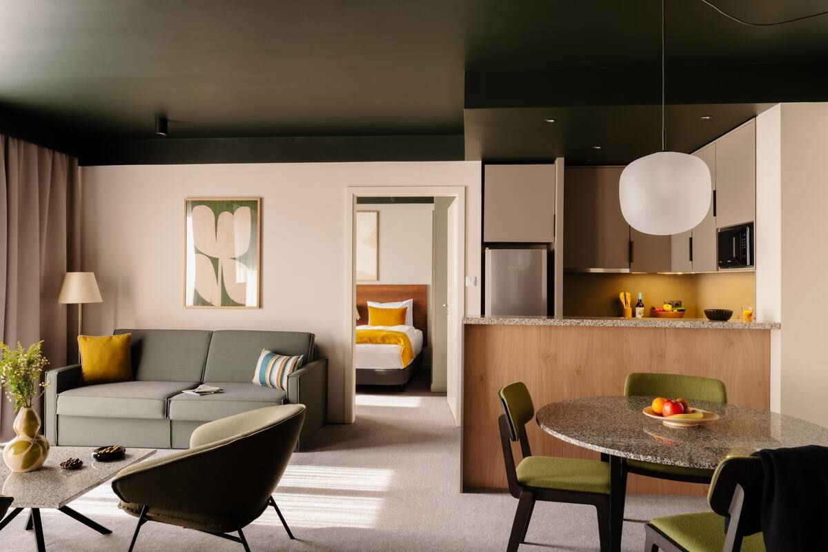 Une chambre d’hôtel moderne comprenant un espace de vie, une table à manger, une cuisine et une chambre à coucher séparée.
