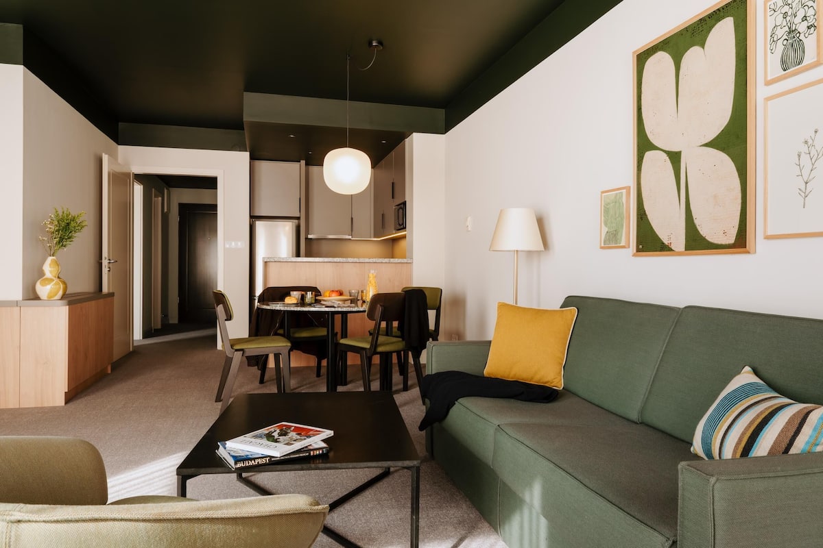 Un salon moderne avec un canapé vert, une table basse et un coin repas avec des chaises.