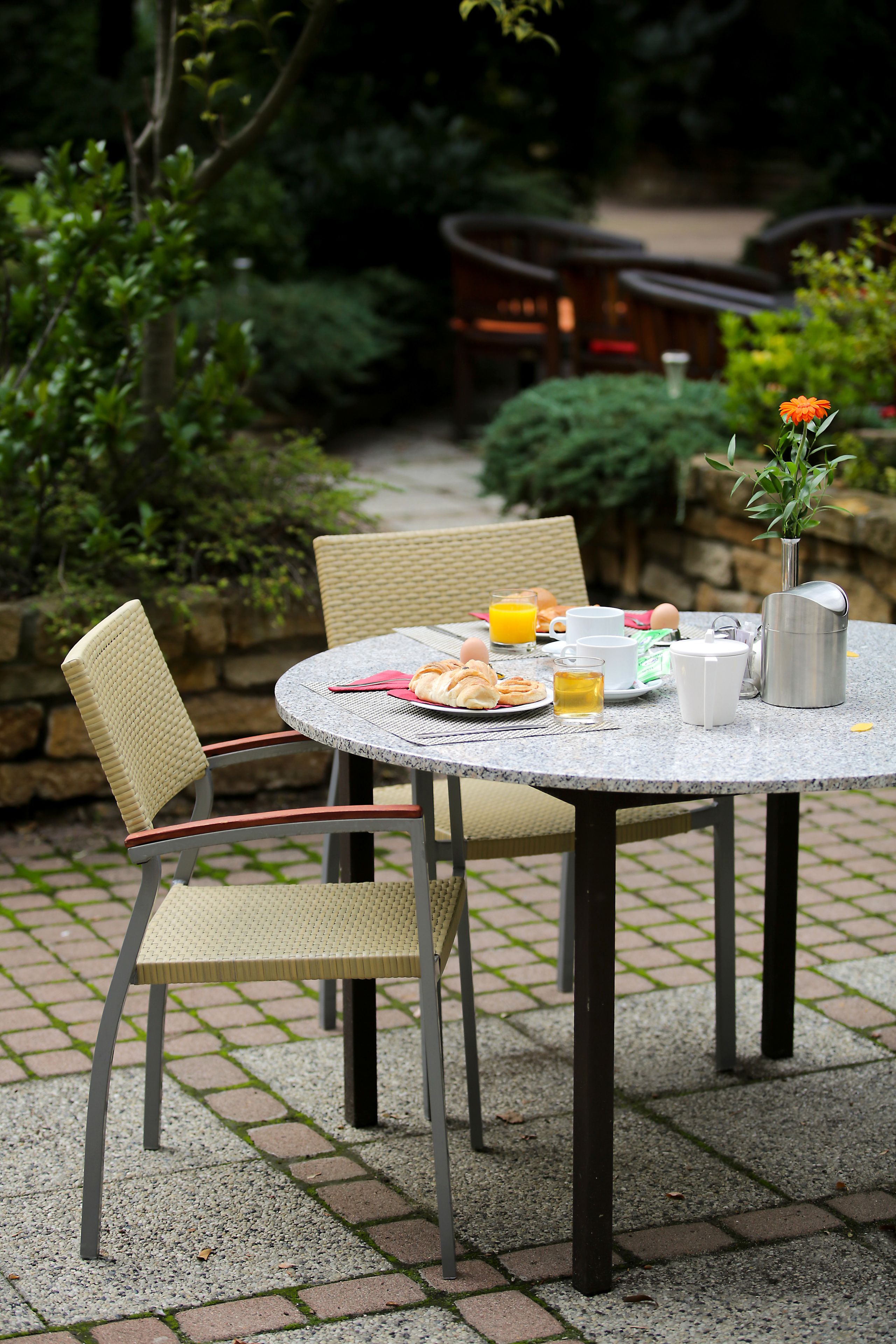 A round table with chairs, breakfast items, and a vase with flowers.