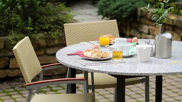 A round table with chairs, breakfast items, and a vase with flowers.
