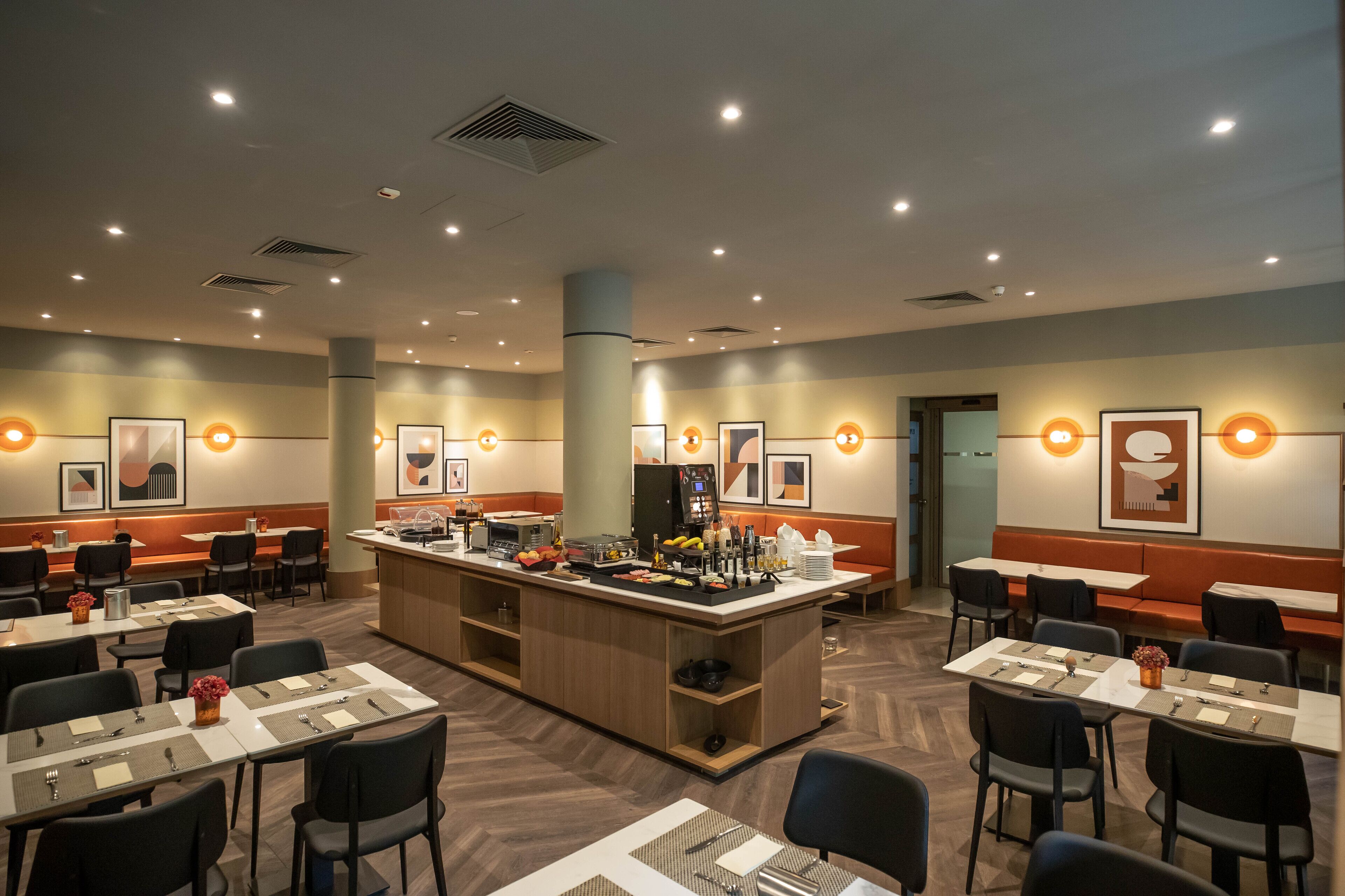 A hotel dining area with multiple tables, a central bar, and artwork on the walls.
