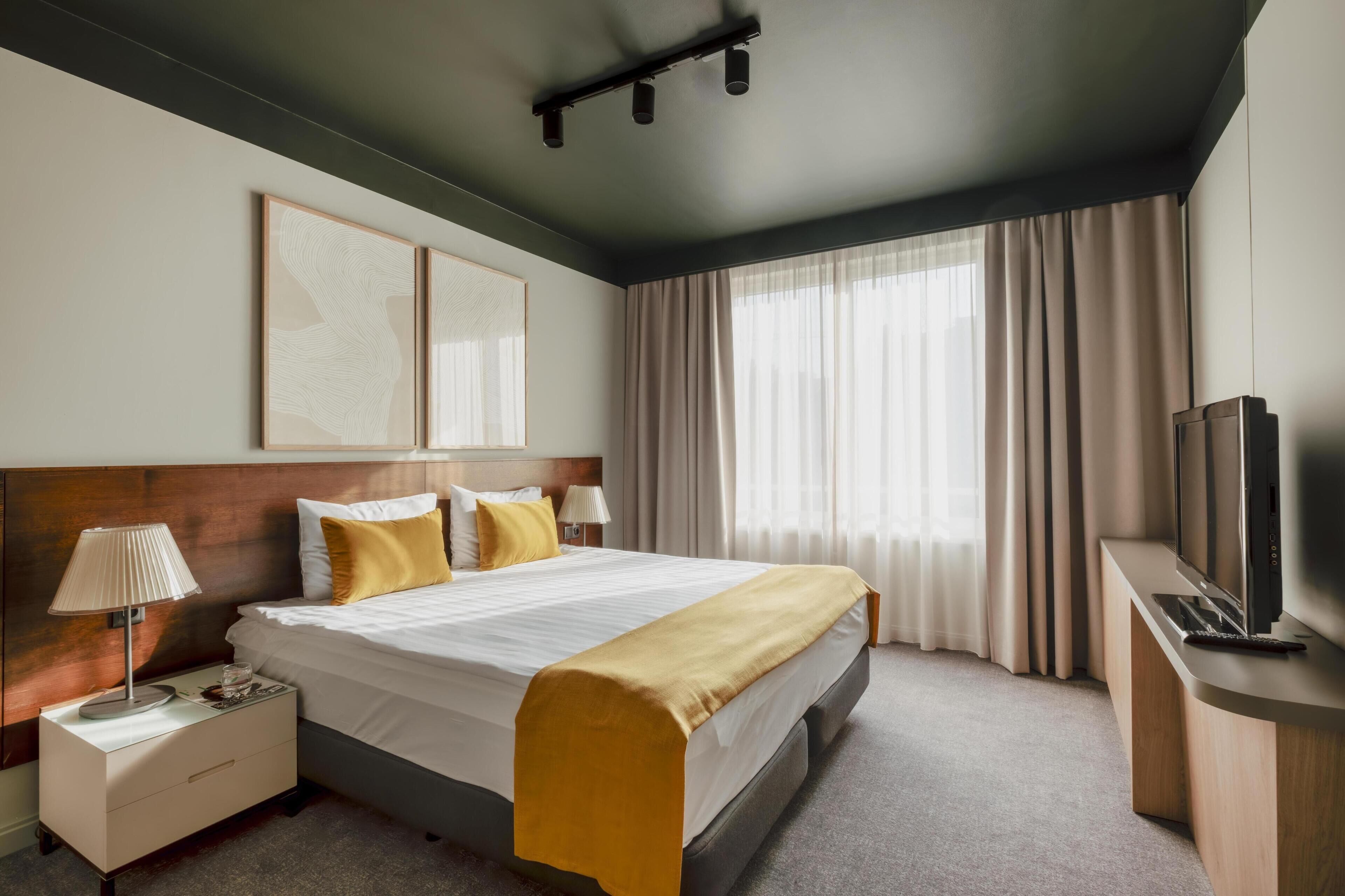 Une chambre d’hôtel avec un lit, une table de chevet, une lampe, une télévision et des rideaux.