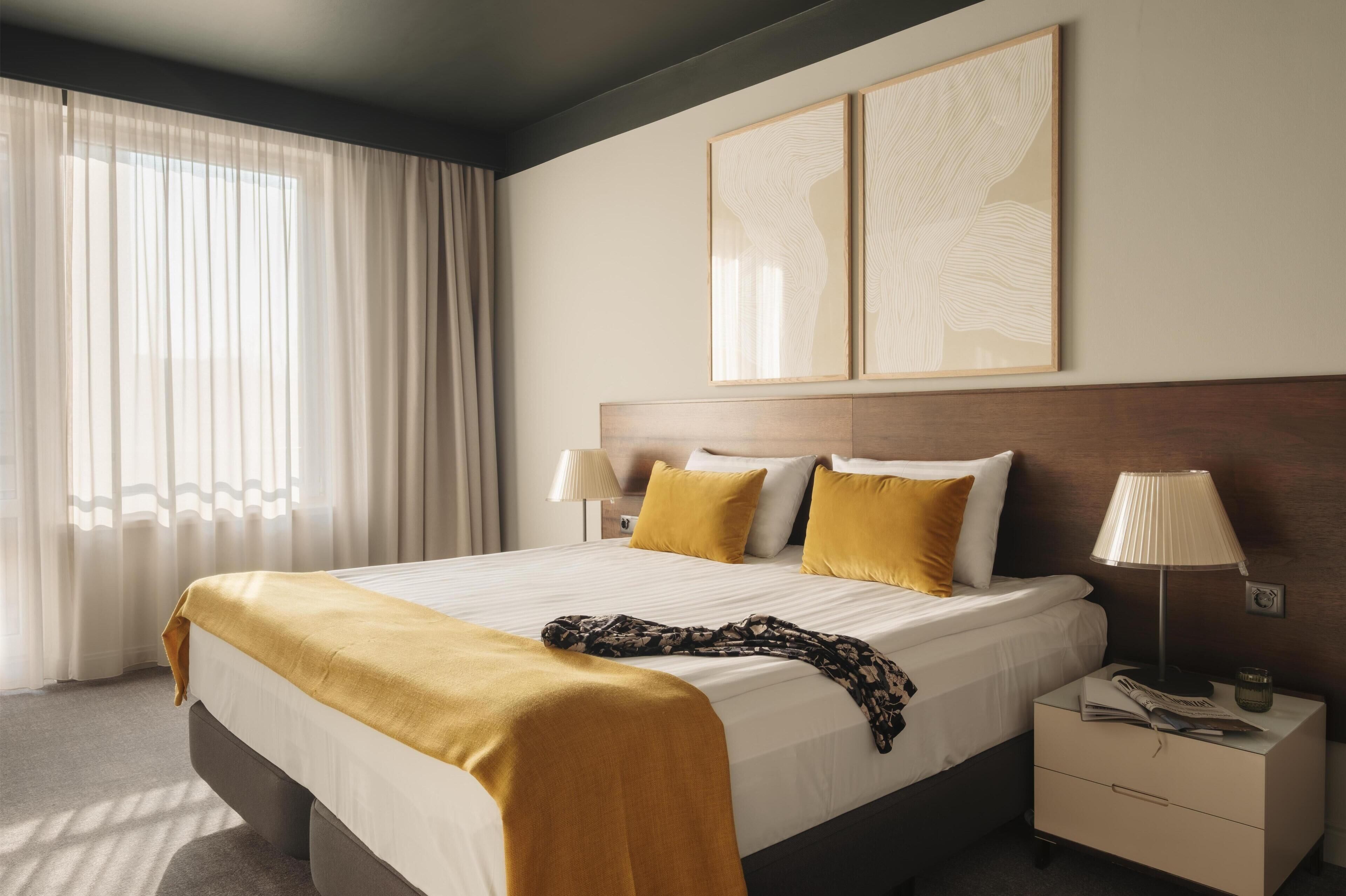 A hotel room with a bed, a nightstand, a lamp, and two wall art pieces.