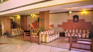 A lobby with striped sofas, wooden furniture, and a staircase. - ECKO Premier Vishnupriya (Udaipur)