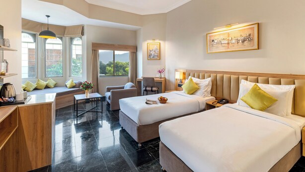 A hotel room with two beds, a desk, a chair, and a window seat. - ECKO Premier Vishnupriya (Udaipur)