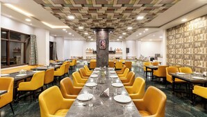 A spacious dining area with yellow chairs and a long table, featuring a patterned ceiling and a marble floor. - ECKO Premier Vishnupriya (Udaipur)