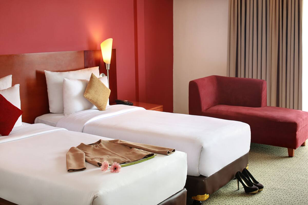 Une chambre d’hôtel avec deux lits, un fauteuil rouge et une table de chevet avec une lampe.