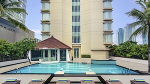 Una piscina con sillas de descanso y un pabellón, rodeada de edificios altos y vegetación.