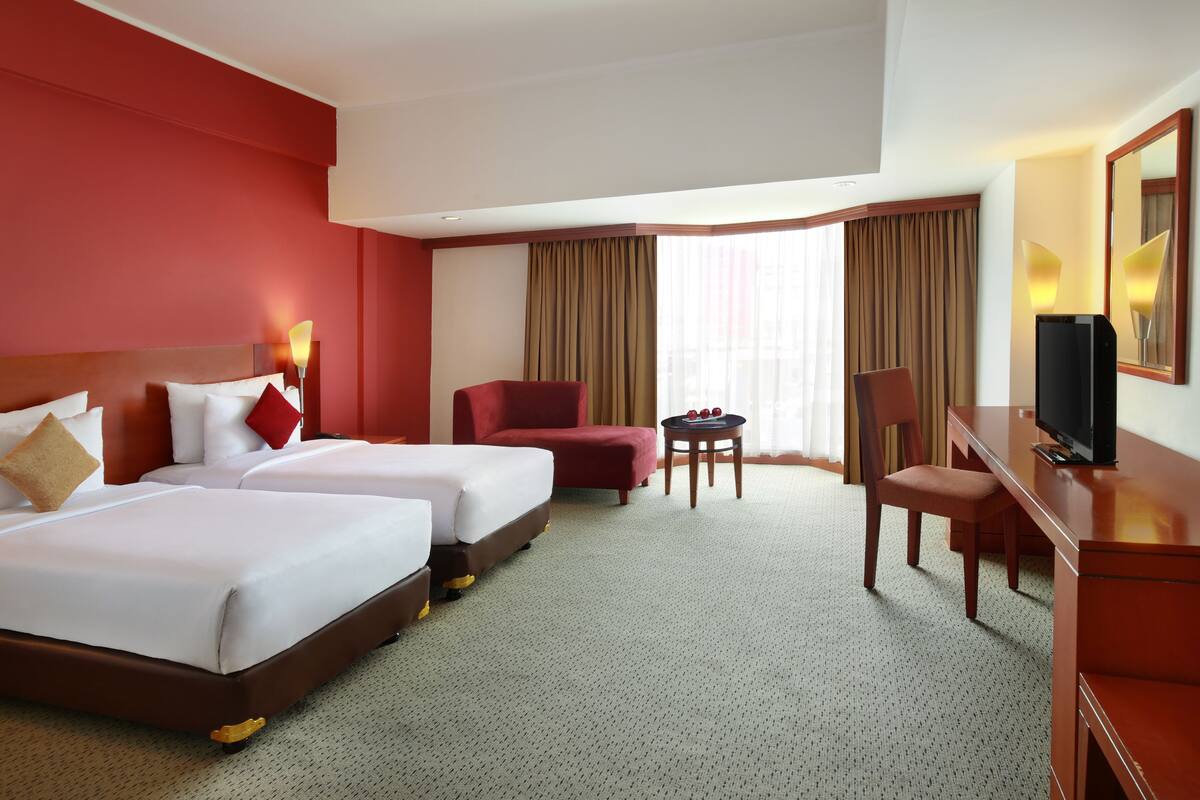 Une chambre d’hôtel avec deux lits, un bureau, une chaise et un téléviseur.
