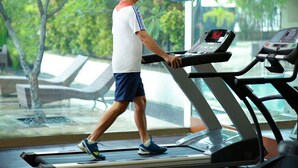Un hombre camina sobre una caminadora en un gimnasio con vistas a la vegetación exterior y sillones de descanso.