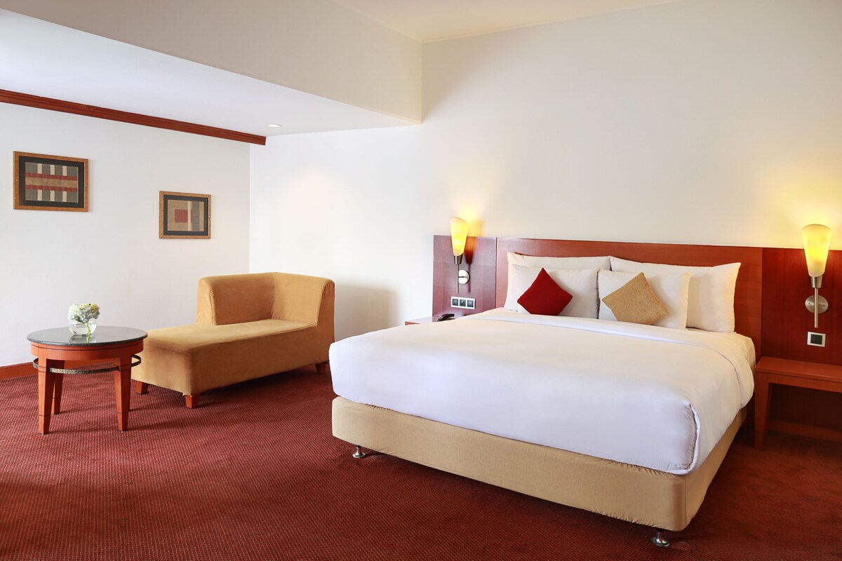 Habitación de hotel con una cama grande, una silla, una mesita pequeña y dos lámparas fijadas a la pared.
