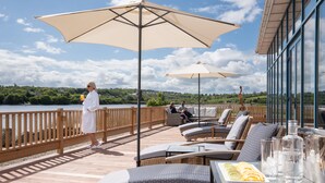Terraza con mobiliario exterior, sombrillas y una mesa con bebidas y una bandeja de frutas.