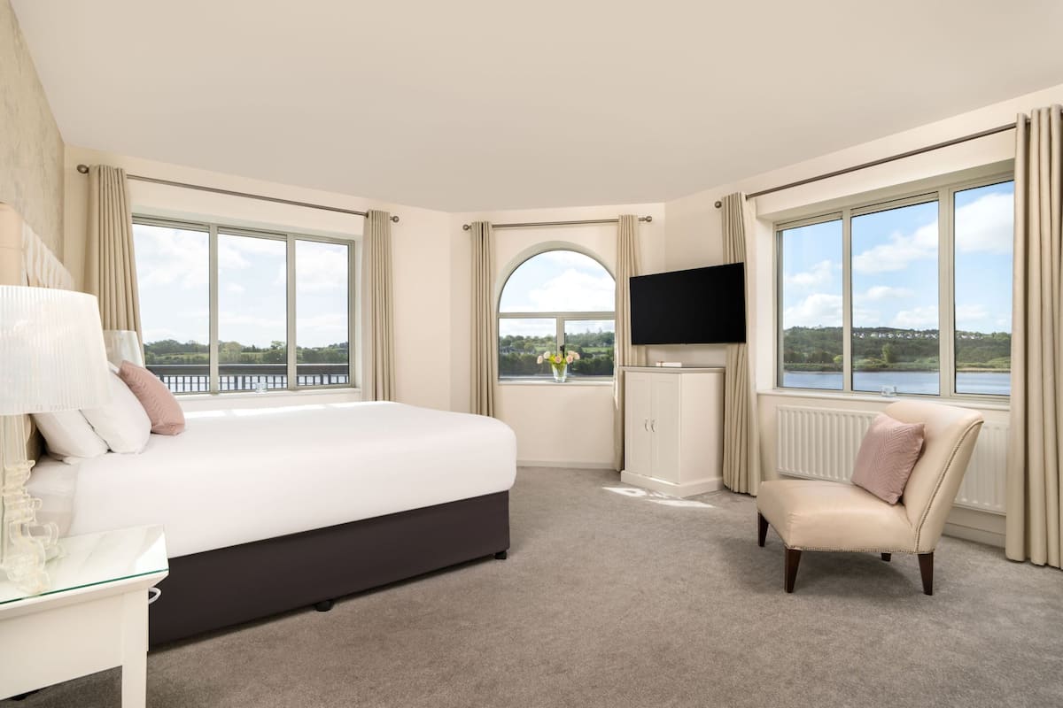A hotel room with a large bed, a TV, a chair, and a view of a lake.