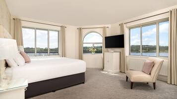 Habitación de hotel con una cama grande, televisión, una silla y vista a un lago.