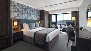 Habitación de hotel con una cama grande, un escritorio y vistas a la ciudad.
