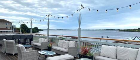 A deck with wicker furniture, string lights, and a view of a river.
