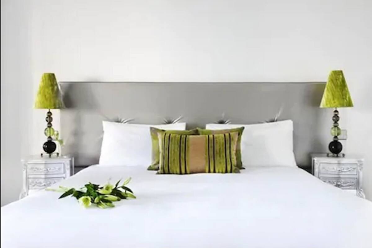 Una cama bien hecha con sábanas blancas y almohadas a rayas verdes, flanqueada por dos mesitas de noche con lámparas.
