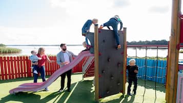 Explore the playground with a climbing structure and slide, surrounded by a tranquil body of water and open sky.