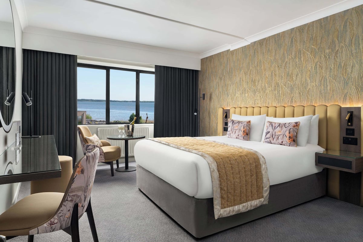 A modern hotel room with a large bed, a desk, and a view of the sea.