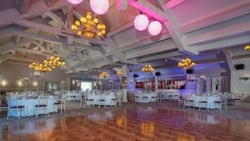Un amplio salón con varias mesas redondas dispuestas para cenar, candelabros y una zona de bar.