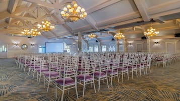 A large hall with rows of white chairs and purple cushions, chandeliers, and a carpeted floor.