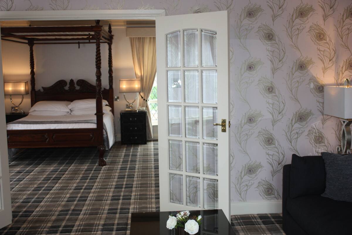 A bedroom with a four-poster bed, a plaid-patterned floor, a white door with glass panels, and a floral wallpaper design.
