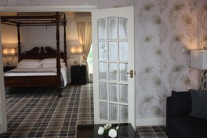 A bedroom with a four-poster bed, a plaid-patterned floor, a white door with glass panels, and a floral wallpaper design.