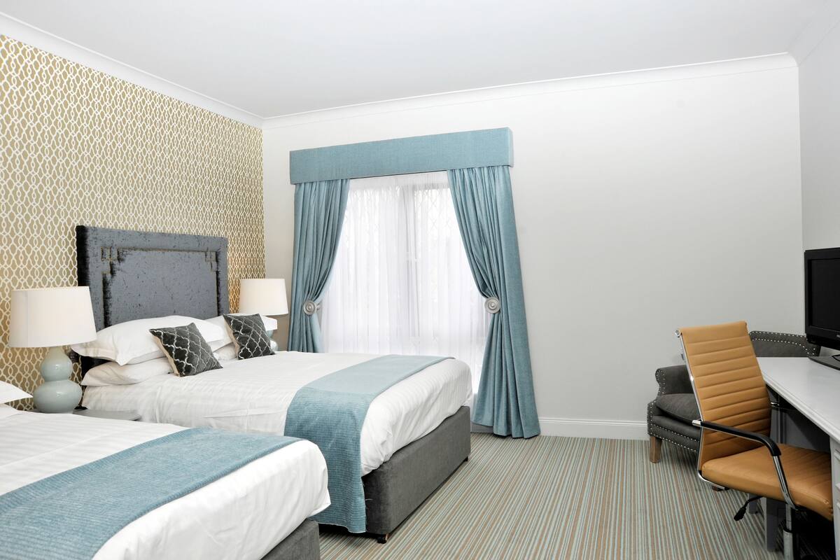 A hotel room with two beds, a desk, a chair, and a television.