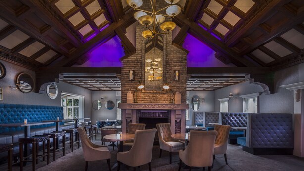 A restaurant with a high ceiling, exposed wooden beams, and a brick fireplace. There are several tables and chairs arranged for dining. - Treacys Oakwood Hotel (Shannon)