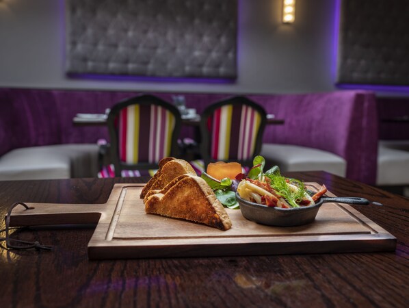 A wooden table with a sandwich and a bowl of salad. There are chairs with striped cushions in the background.