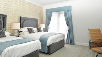 A hotel room with two beds, a large window with blue curtains, a single chair, and a patterned wallpaper.