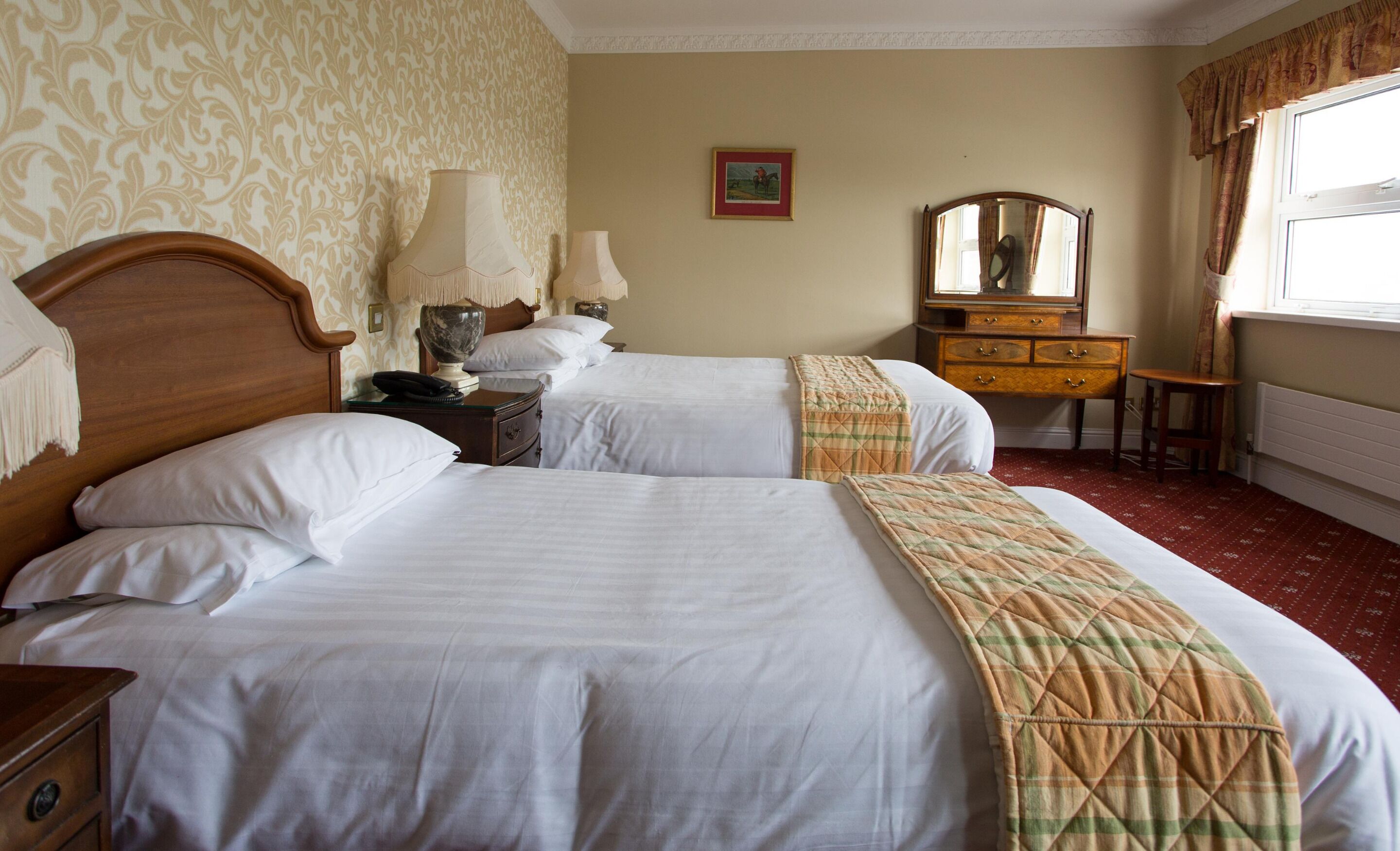 Une chambre d’hôtel avec deux lits, une commode en bois, un miroir et un tableau encadré au mur.