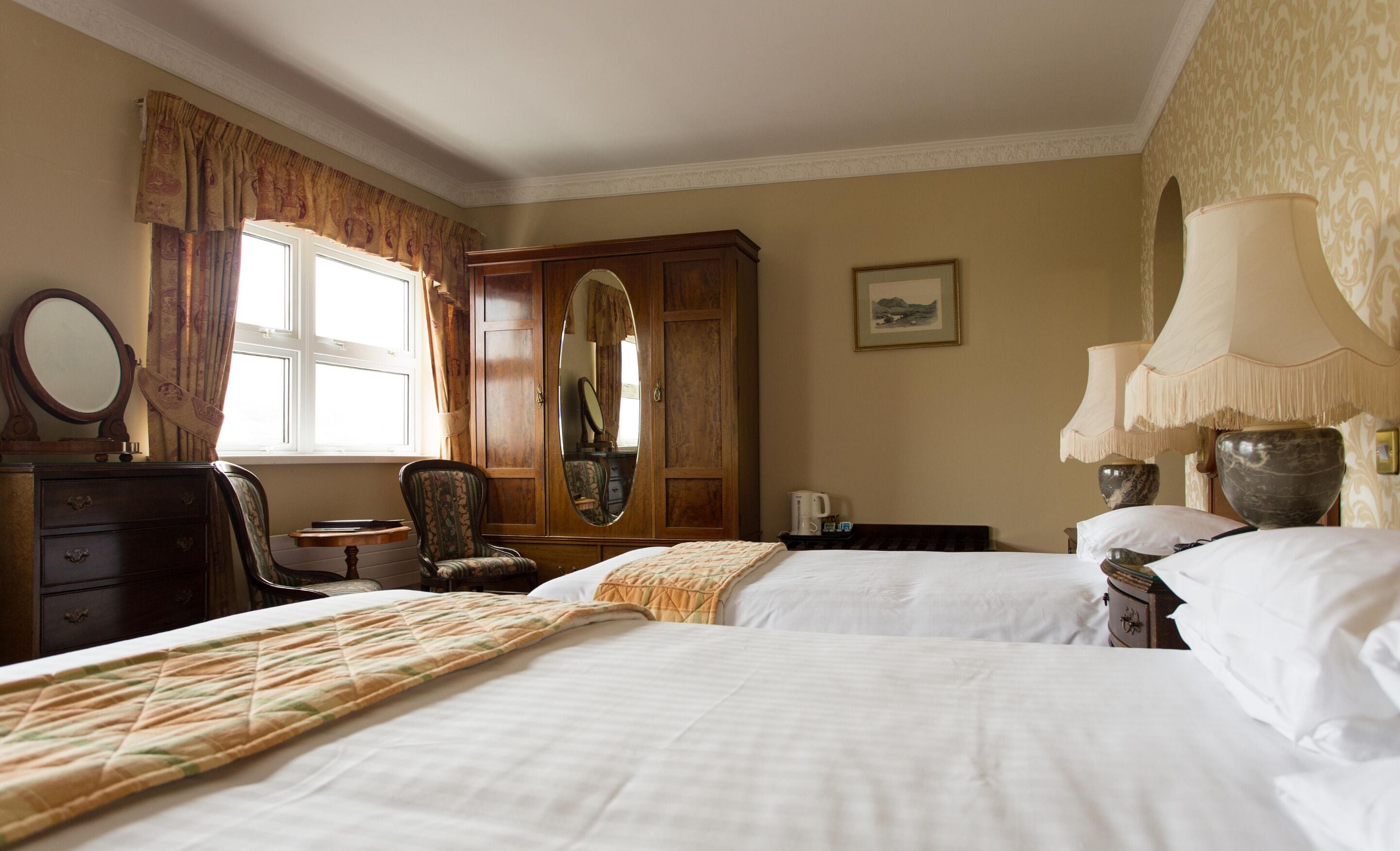 Une chambre d’hôtel avec deux lits, une armoire en bois, une chaise, un bureau avec une lampe et une fenêtre avec des rideaux.