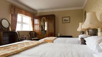 Une chambre d’hôtel avec deux lits, une armoire en bois, une chaise, un bureau avec une lampe et une fenêtre avec des rideaux.