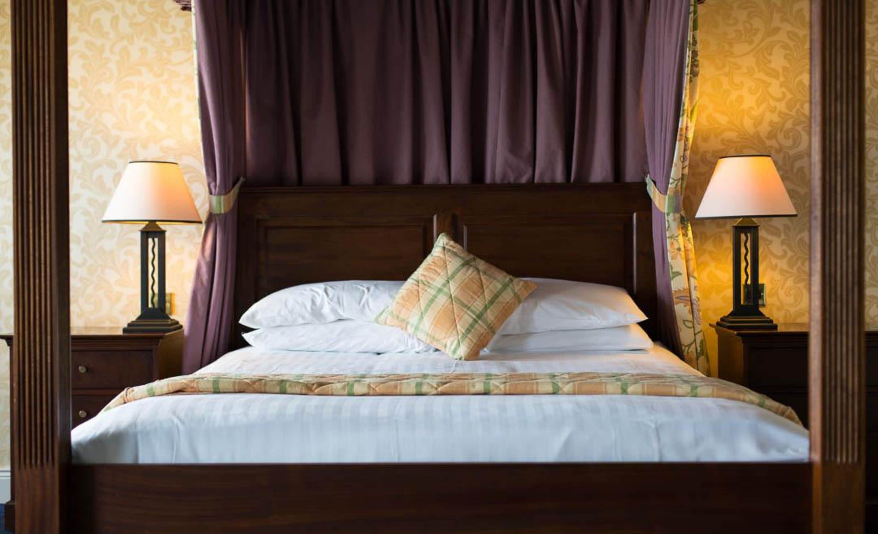 A neatly made bed with a plaid pillow, two bedside lamps, and a wooden headboard.