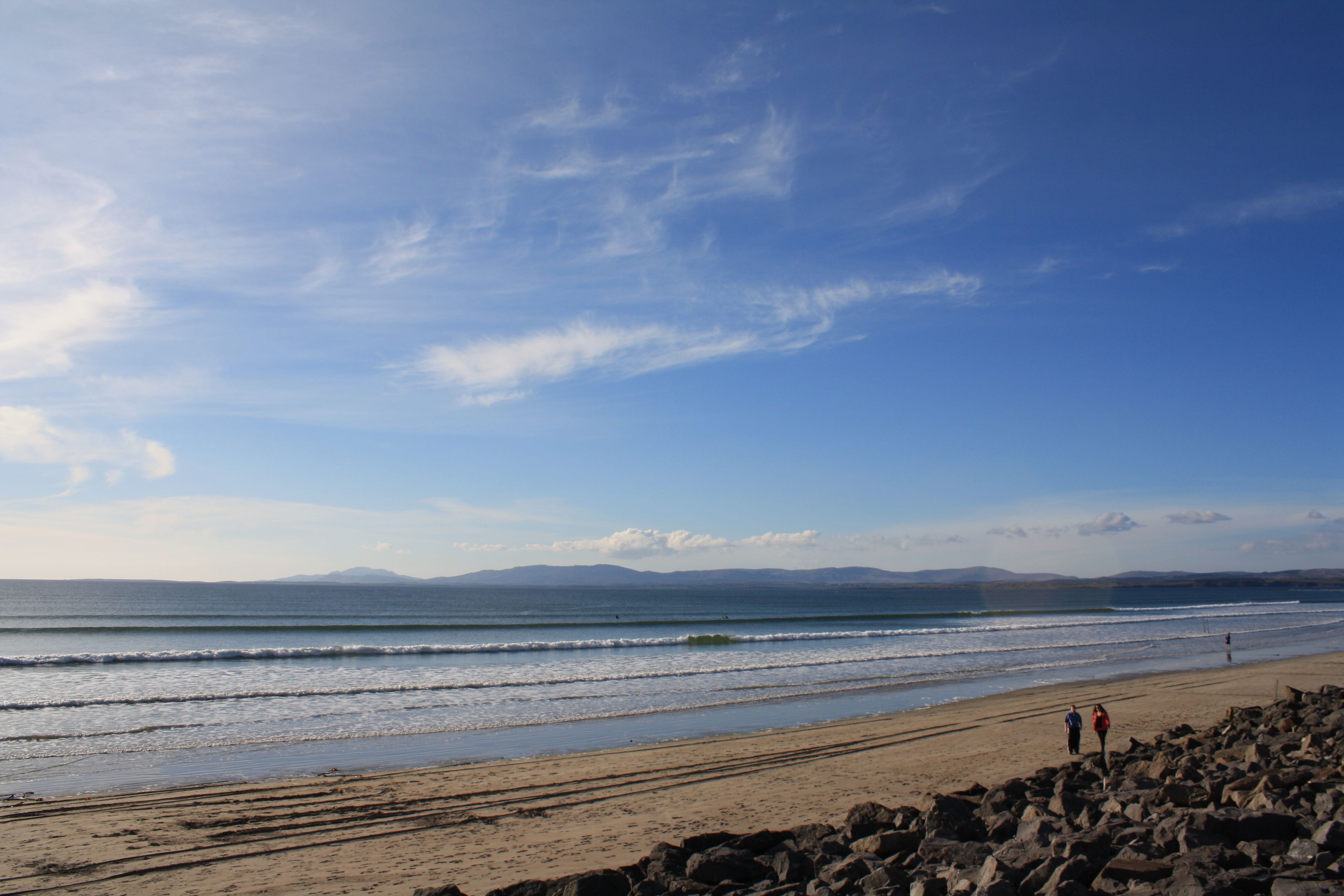 A beach with rocky terrain, a clear sky, and a distant mountain range.