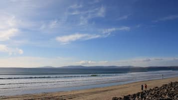 A beach with rocky terrain, a clear sky, and a distant mountain range.