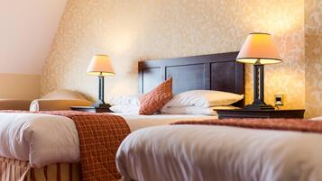 A hotel room with two beds, each with a bedside table and lamp, and a patterned wallpaper.