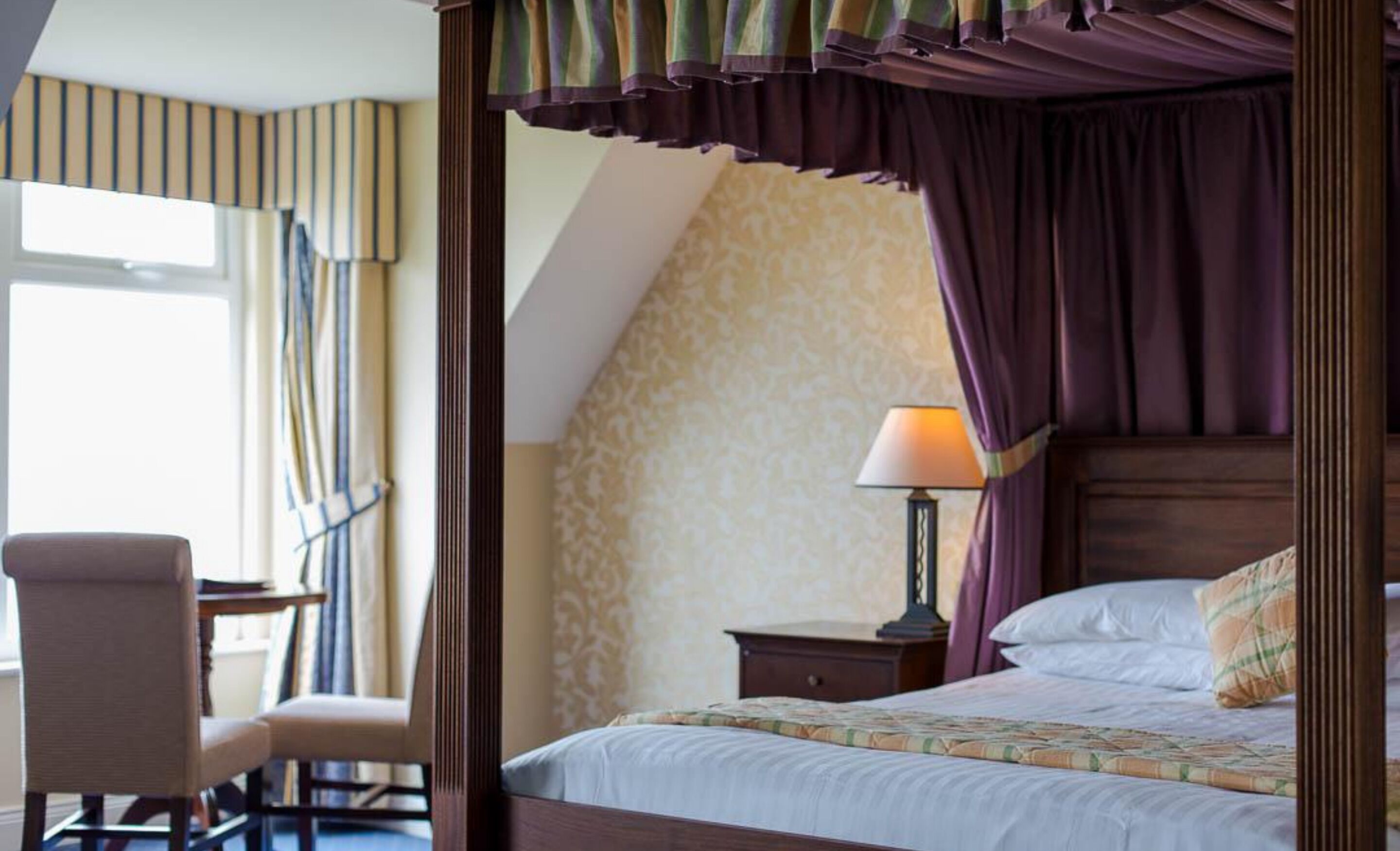 A bedroom with a four-poster bed, a desk, and a chair.