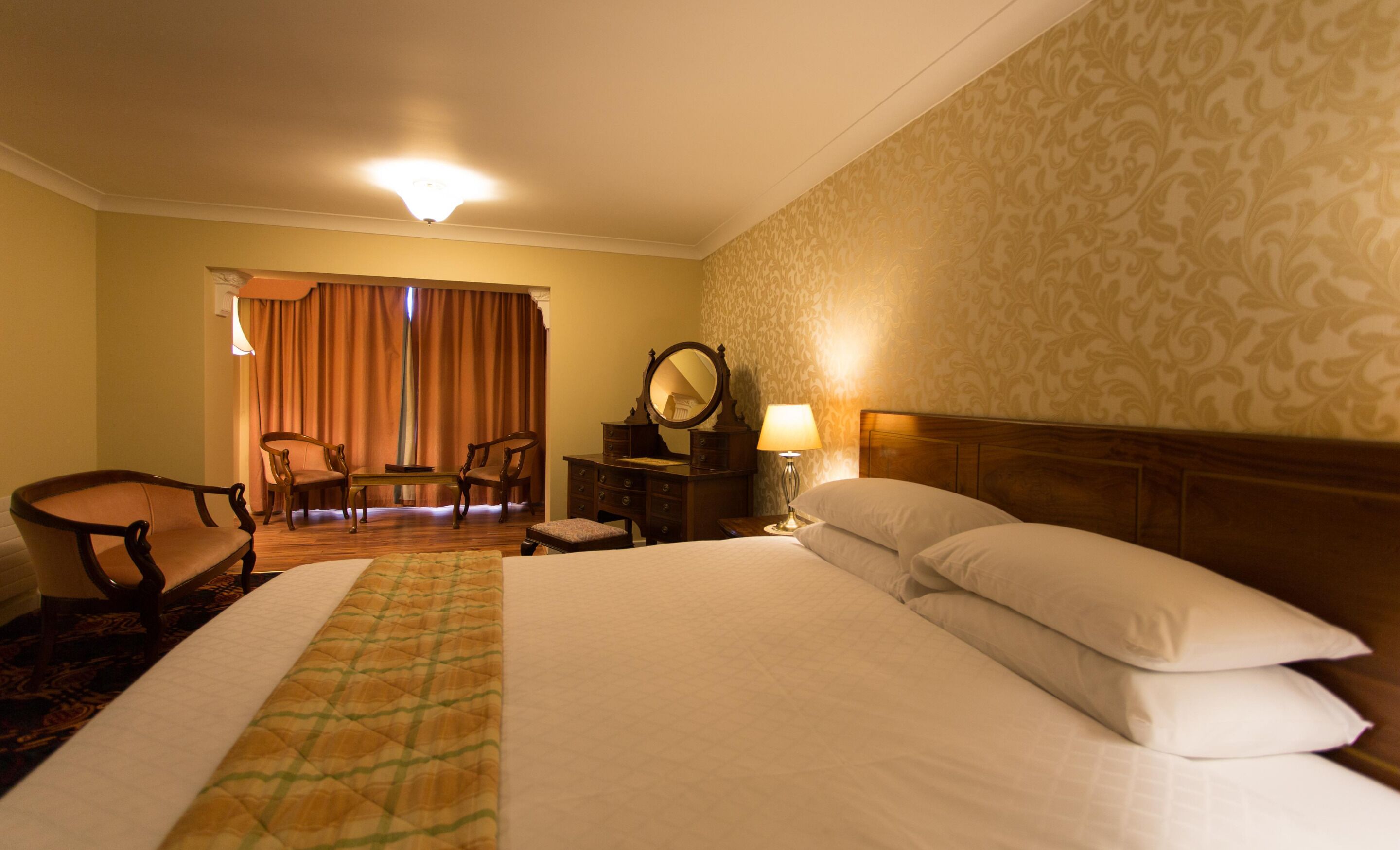 Habitación de hotel con cama, escritorio, silla, lámpara y ventana con cortinas.