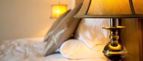 A close-up of a bed with white bedding, a lamp, and a wall-mounted light fixture.
