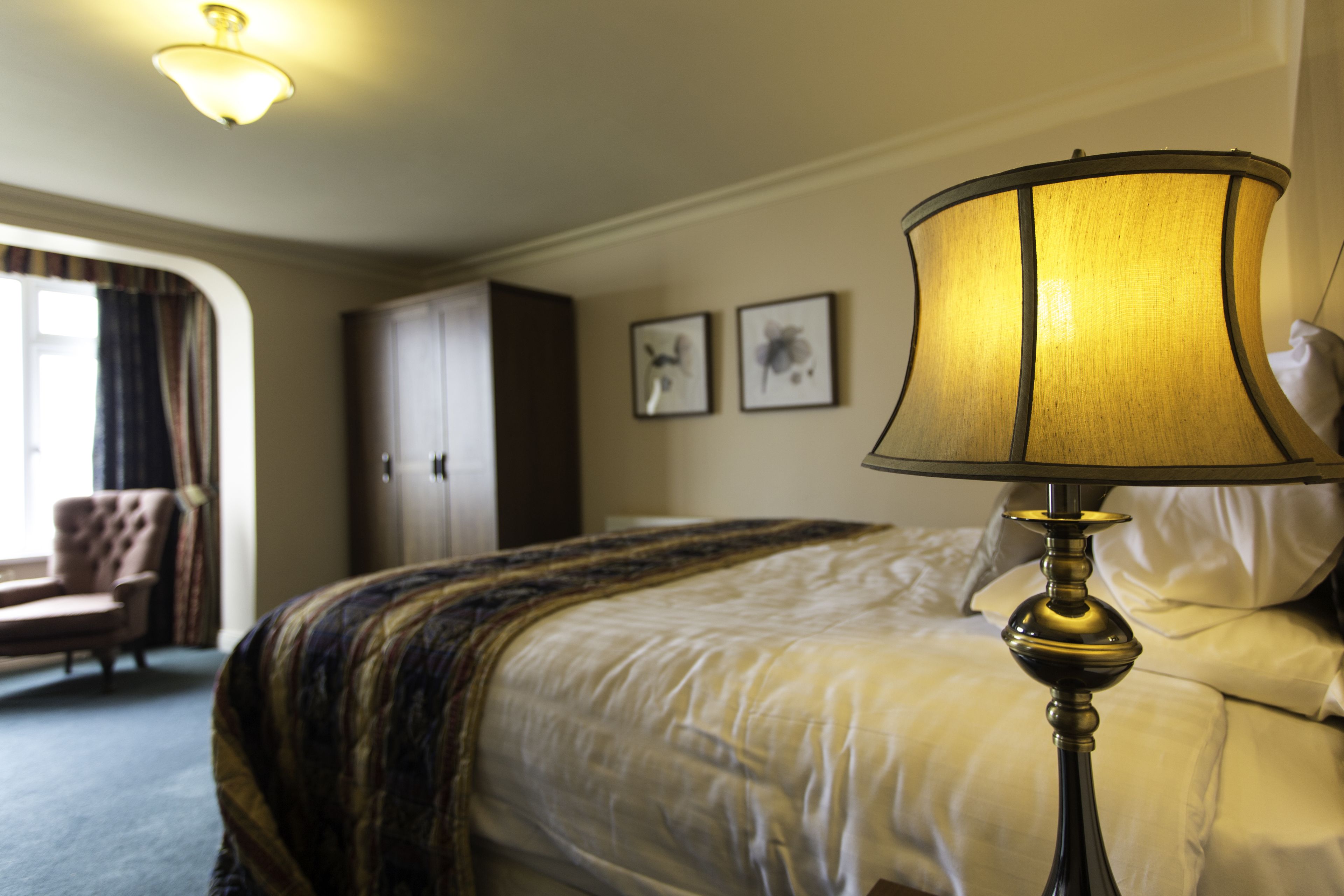 Quarto de hotel com uma cama, uma luminária, um guarda-roupa e duas quadros na parede.