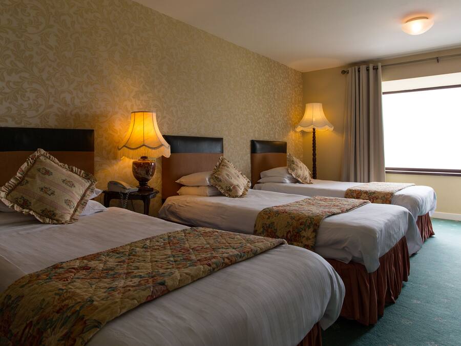 Habitación de hotel con tres camas, cada una con cabecera, lámparas de noche y ropa de cama con estampado floral.