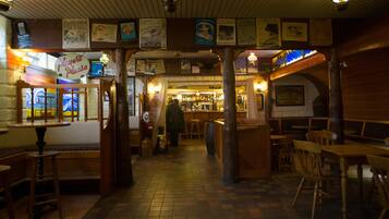 A cozy bar area with wooden furniture, a visible bar counter, and various posters on the walls.