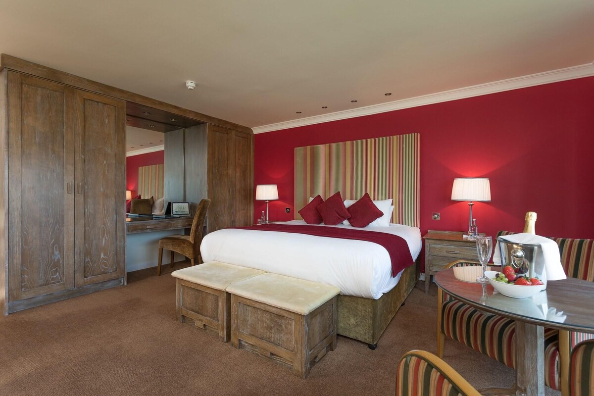 Habitación de hotel con una cama grande, un escritorio, una silla y una mesa de comedor con un cuenco de fruta.