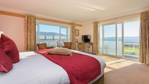 A hotel room with a large bed, a desk, a television, and a balcony with a view of the sea. - Connemara Coast Hotel (Galway)