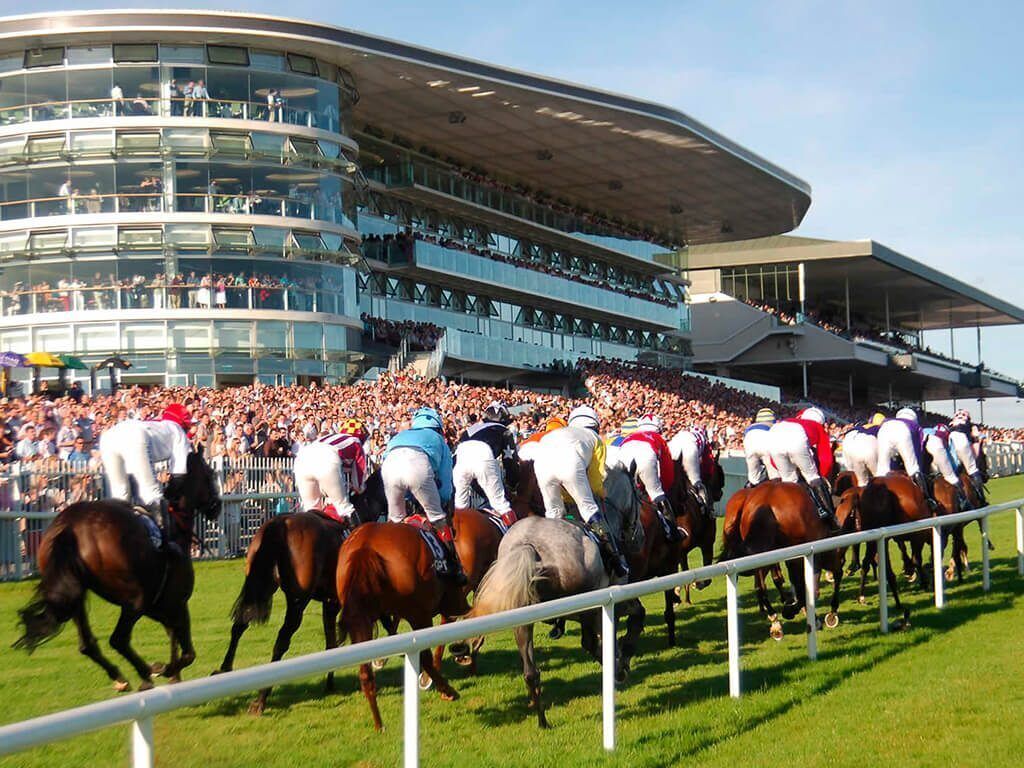A horse race with jockeys on horses, a crowd of spectators, and a modern stadium with multiple levels of seating.