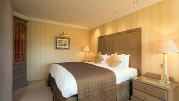 A neatly arranged bedroom with a large bed, a bedside table with a lamp, a wooden wardrobe, and a framed picture on the wall.